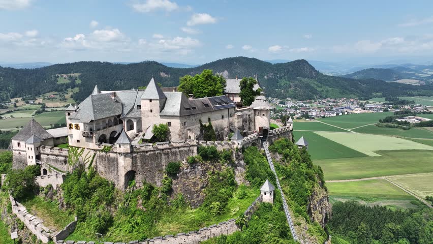 Cinematic drone footage capturing Hochosterwitz Castle on hilltop, fortified walls, dramatic cliffs, summer colors, sweeping aerial movement, historical landmark atmosphere