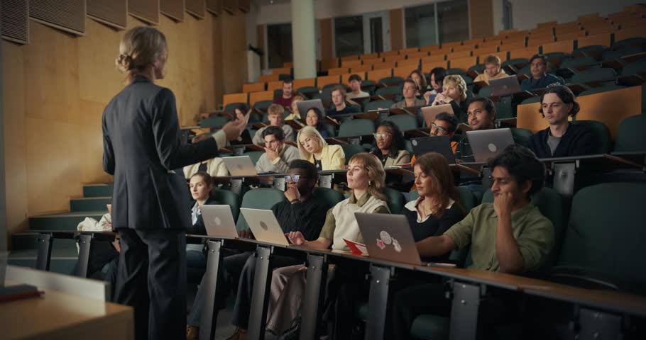 Female Professor in a Dark Suit Delivers an Interactive Lecture to a Diverse Group of University Students Using Laptops, as Multicultural Men and Women Listen, Modern Higher Education