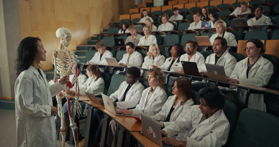 Anatomy Lecturer in Lab Coat Uses a Skeleton Model to Explain Bones and Muscles, Medical Education Prepares Students for Careers in Surgery, Medicine, Neuroscience, Biomedicine in a University Theater