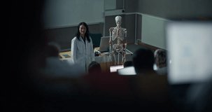 Medical Professor in White Lab Coat Explains Human Skeletal Anatomy of Skeleton Model, While Diverse University Students in Lecture Hall Follow on Laptops, Healthcare Science Classroom Presentation - Powered by Shutterstock - Get 15% off with code: PIKWIZARD15