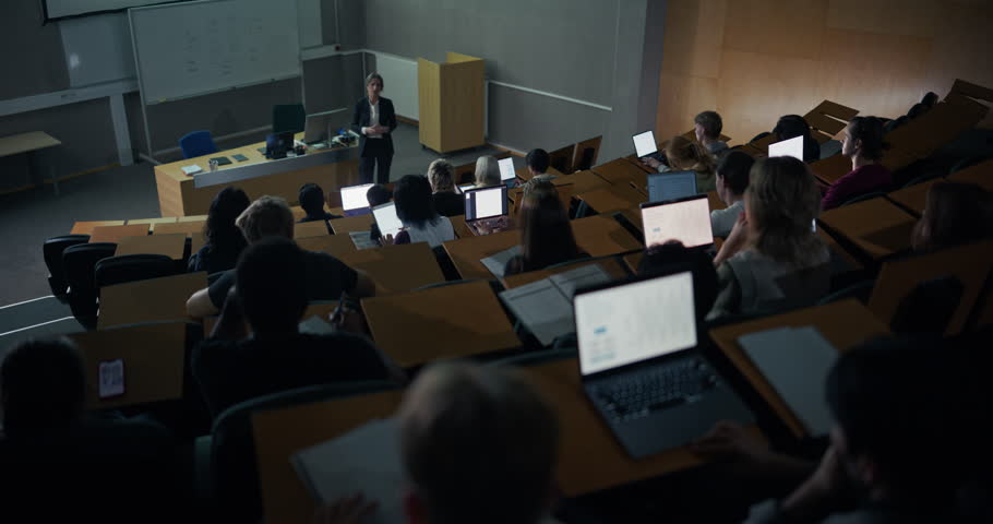 Overhead View of a University Lecture Female Lecturer Explains Advanced Computer Science Concepts While Students in Classroom Follow Slides, Type on Laptops, Take Notes