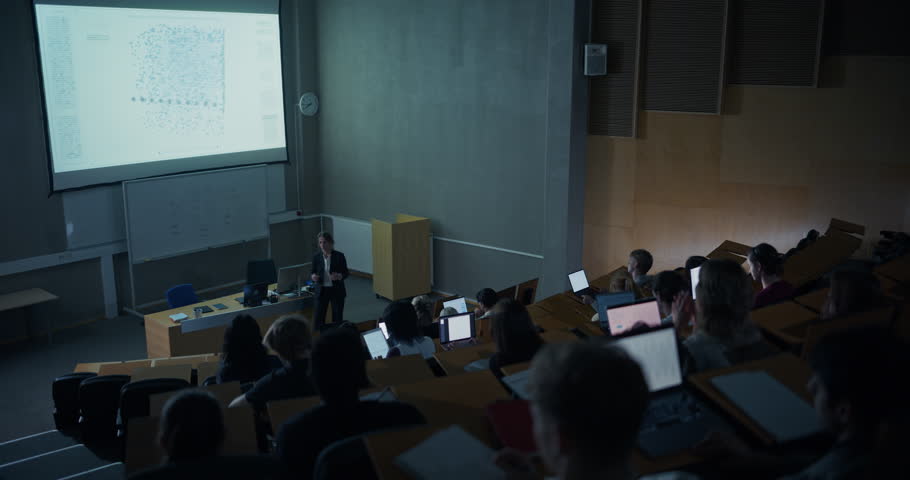Wide Shot of University Auditorium Where Female Professor Delivers an Computer Science Lecture on Complex Data Visualization as Diverse College Students Follow Along on Laptops, Analyze Code