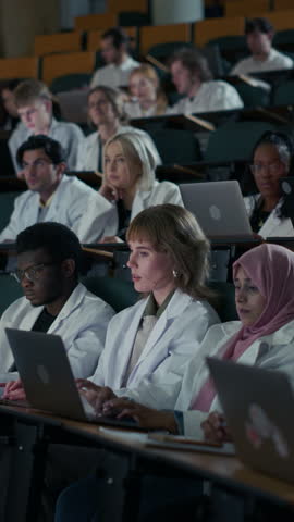 Vertical Classroom Video of Diverse Male and Female Medical Students, Black, White, and Middle Eastern Undergraduates, Quietly Listening, Typing on Laptops, and Writing Notes, Intensive Lecture Study