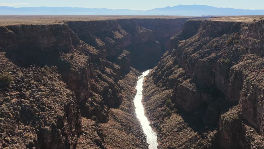 High-angle aerial view capturing the deep, winding channel of the Rio Grande River cutting through the massive geological canyon walls. Highlights the arid beauty of the American Southwest.