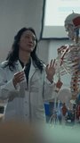Vertical Video: Female Anatomy Professor Guiding Medical Students Through Skeletal Anatomy, Using a Colorful Model to Highlight Bone Landmarks, Muscle Attachment, University Teaching - Powered by Shutterstock - Get 15% off with code: PIKWIZARD15