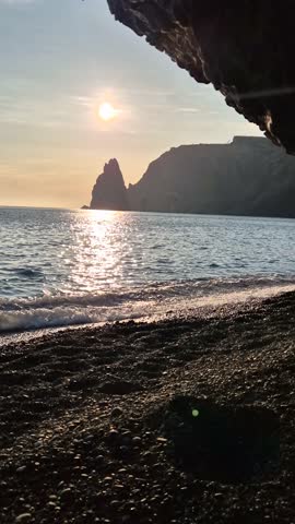Beach Sea Sunset Ocean waves glittering water reflects sun over rocky shore and distant cliff landscape during golden hour Vertical video