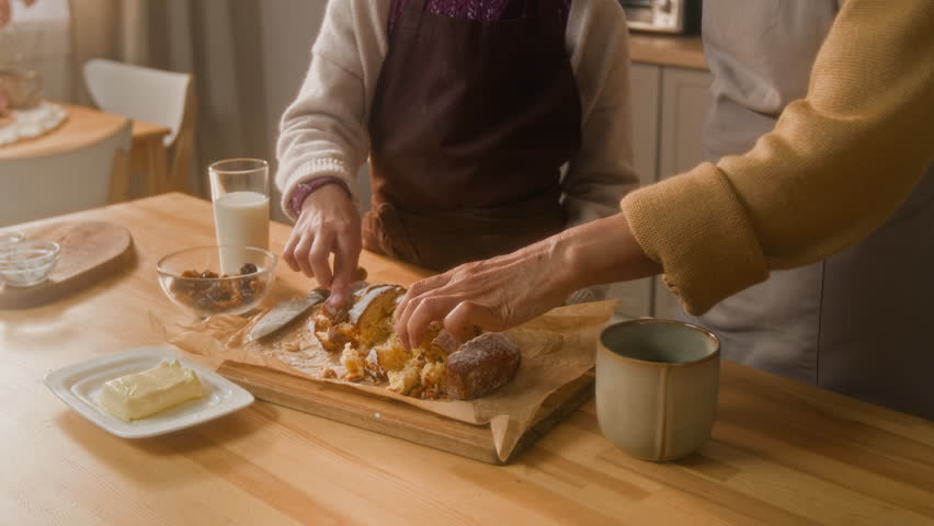 Tilt up shot of happy pre-teen girl and senior grandmother eating freshly baked loaf cake and high fiving at home kitchen
