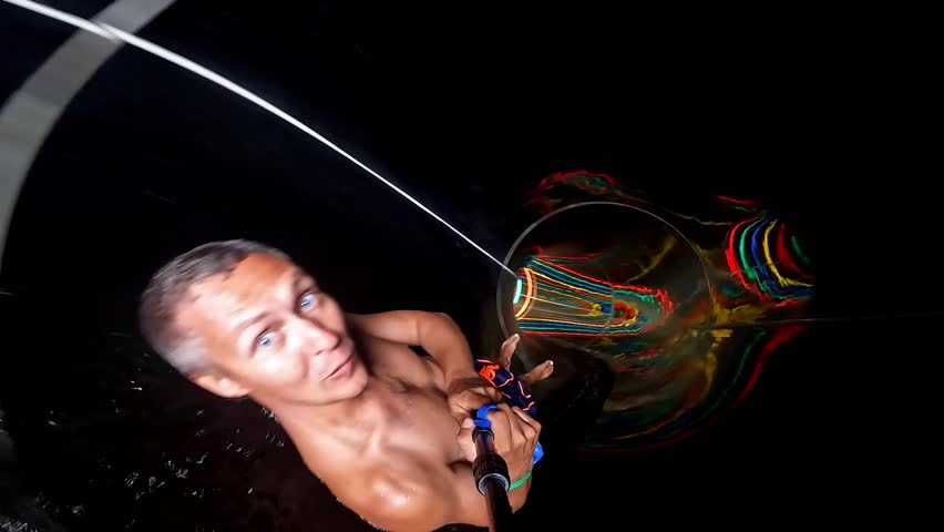 A man with an action camera is racing along the neon tube of a water slide, bright rings of light create a futuristic effect and a feeling of extreme.