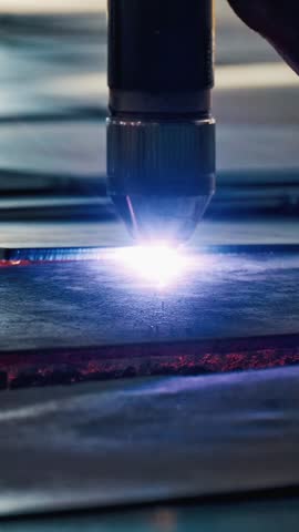 Industrial CNC laser cutting machine processing metal sheet with bright sparks and plasma light. High precision manufacturing technology in modern metalworking industry