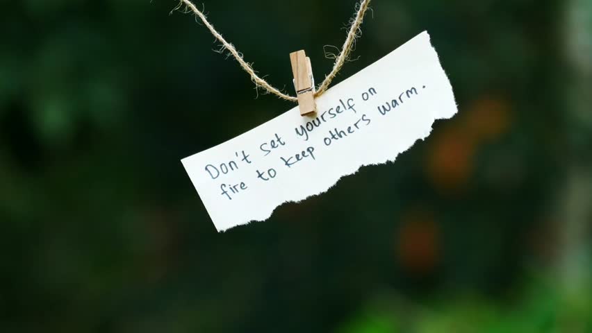 Inspiring self-care quote handwritten on torn white paper pinned to twine, hanging outdoors against a soft green bokeh background under natural daylight.