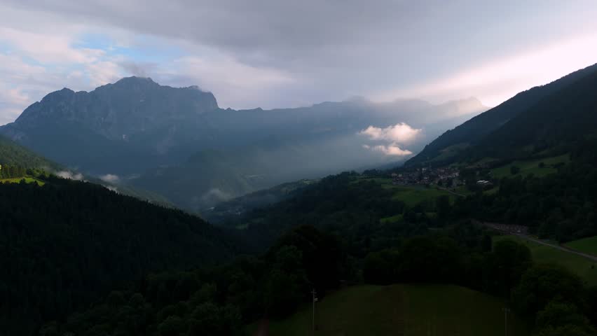 Dramatic aerial sunset in Val di Scalve, Orobie Alps. Sunbeams piercing through clouds over the valley and Presolana peak. Majestic Italian mountain landscape at dusk