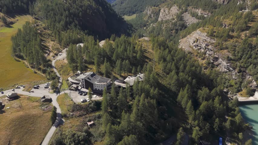 Push in aerial establishing shot of a fancy hotel in pine woodland in Valtournenche, Italy, Aosta Valley, Valle d’Aosta, surrounded by alpine nature