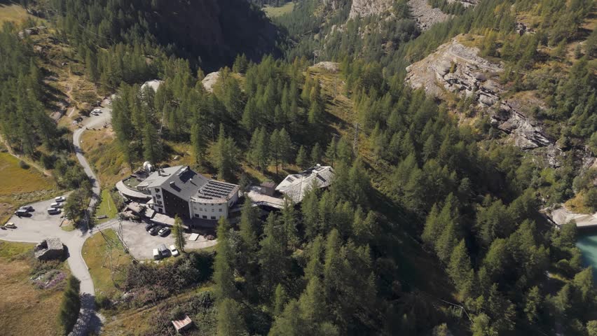 Aerial drone tilt down revealing a fancy hotel in pine woodland in Valtournenche, Aosta Valley, Valle d’Aosta, Italy surrounded by alpine nature