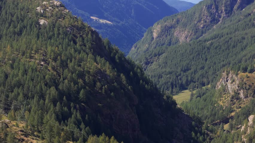 Aerial panning right close-up of pine-covered mountains in Italy, Aosta Valley, Valle d’Aosta, showing an alpine establishing view