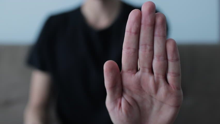 Close-up of a hand gesturing to stop, with a blurred figure in the background indicating denial, rejection, and disagreement