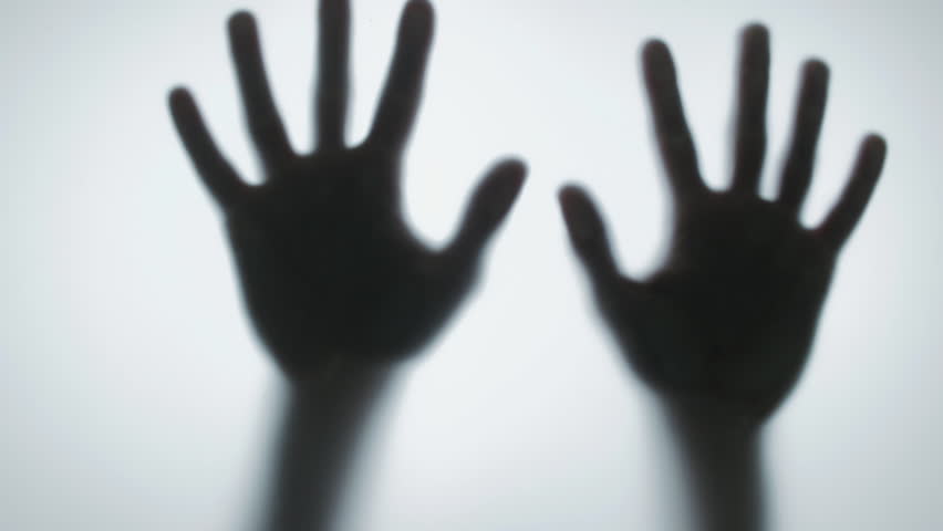 Spooky black silhouette of two hands sliding down a frosted glass surface. Creepy, scary, and mysterious horror concept