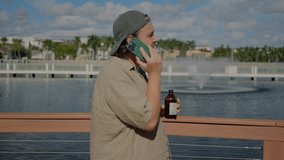 Relaxed modern digital nomad lifestyle, remote work communication in sunny urban park, young man talking on the phone with clients while holding cold brew bottle - Powered by Shutterstock - Get 15% off with code: PIKWIZARD15