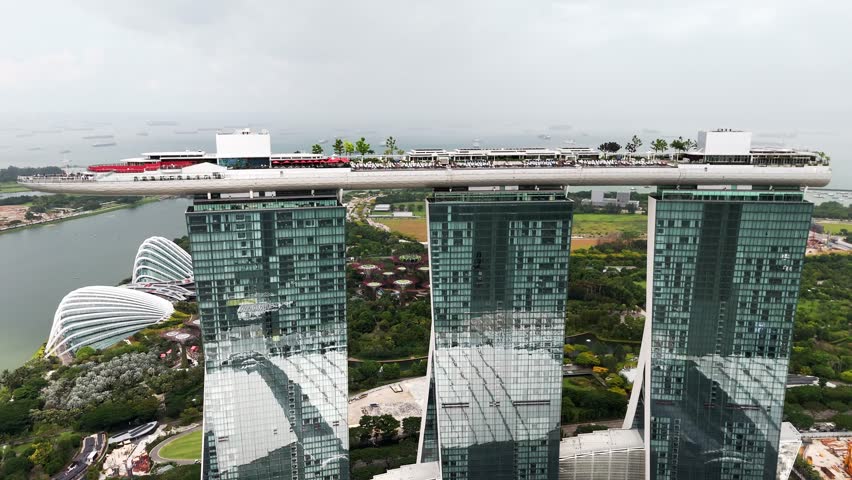 Aerial view of Marina Bay Sands in Singapore, highlighting the iconic SkyPark above three towers, surrounding gardens, calm bay waters, and ships anchored offshore in a global financial city.