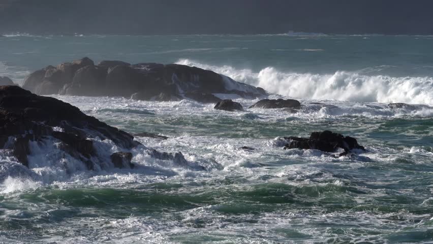 Ocean waves surround dramatic rock formations along the Atlantic shore in sunny weather