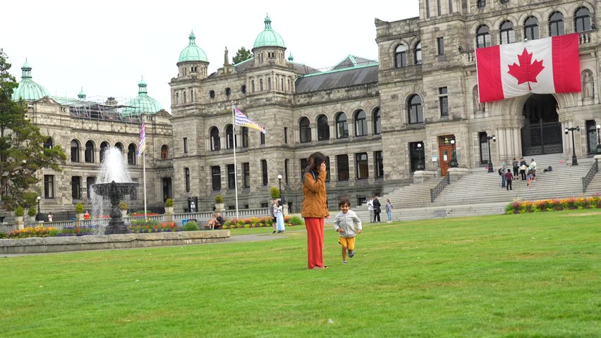 Happy mother and son running together on the lawn in front of the parliament buildings in victoria, british columbia, canada, enjoying a sunny day of sightseeing