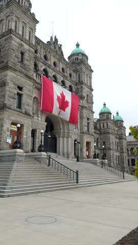 Waving canadian flag highlighting neo baroque british columbia parliament buildings architectural grandeur under bright summer sky in victoria
