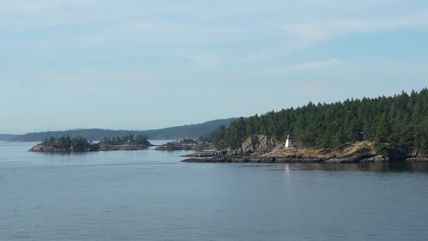 Beautiful summer day with clear skies, calm waters and a ferry approaching vancouver island, passing by an active lighthouse on the rocky coastline