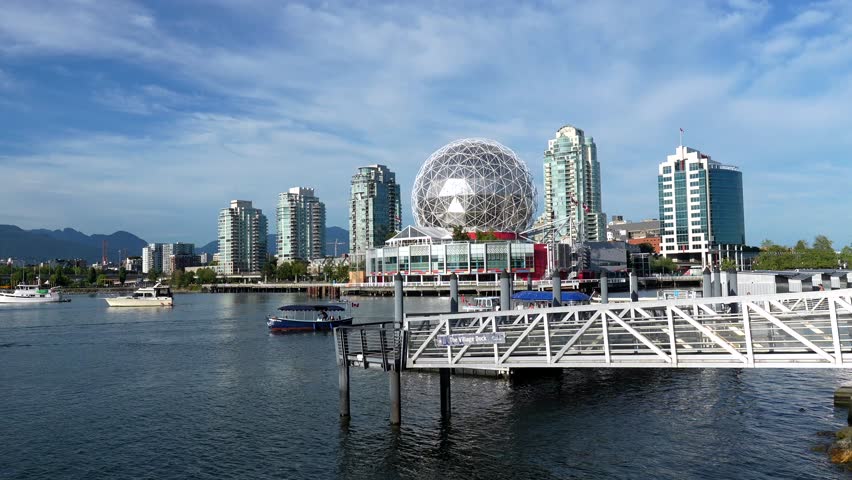 Science world museum standing prominently on false creek shores in vancouver, with ferries traversing waters against modern buildings and distant mountain backdrop