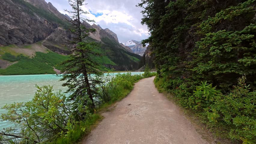 Beautiful turquoise waters of lake louise reflect surrounding mountains and glaciers on a cloudy summer day as seen from the lakeshore trail