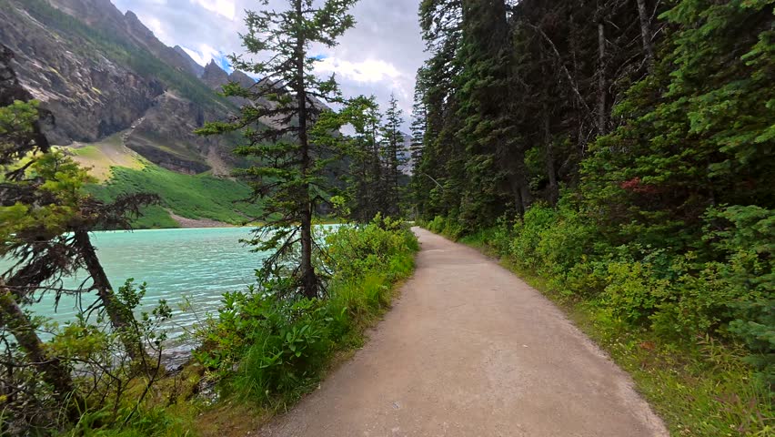 Scenic shoreline trail winding through pristine coniferous forest alongside turquoise waters of lake louise in banff national park. Canadian rockies showcasing natural alpine landscape during summer