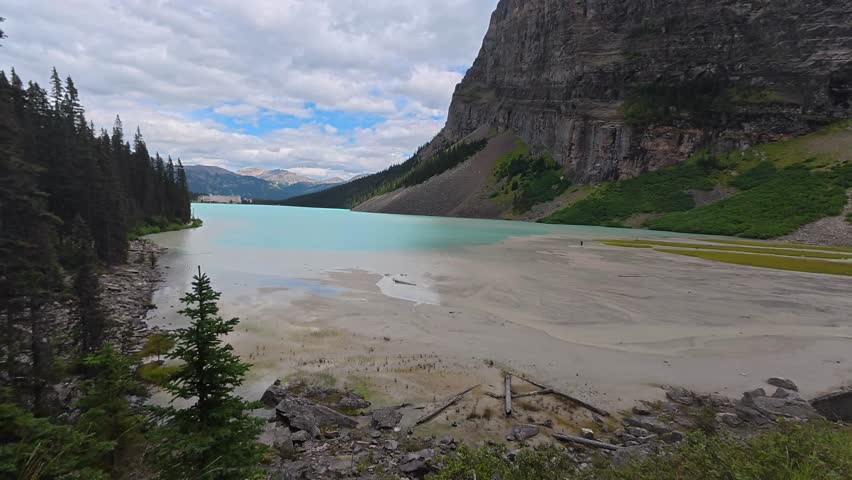 Turquoise waters surrounding sandy shoreline at lake louise, framed by evergreen forest and towering cliffs in banff national park, alberta, creating breathtaking landscape