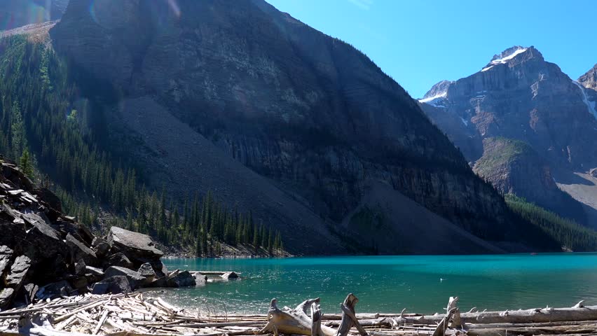 Majestic valley of the ten peaks reflecting in turquoise water of moraine lake in banff national park with tourists walking on driftwood logs on a sunny summer day