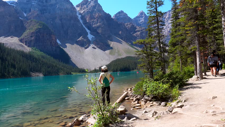 Majestic mountains surround a crystal clear turquoise lake, where a young woman stands on the shore, captivated by the breathtaking beauty of moraine lake in banff national park, alberta, canada