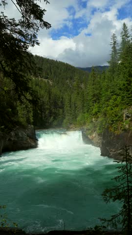 Turquoise water flows powerfully through a forested landscape at overlander falls in jasper national park, showcasing the natural beauty of the canadian rockies