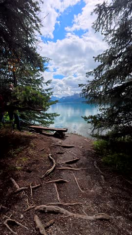 Beautiful panoramic view of maligne lake in jasper national park, featuring a wooden bench under pine trees, turquoise water, and mountain reflections under a cloudy sky