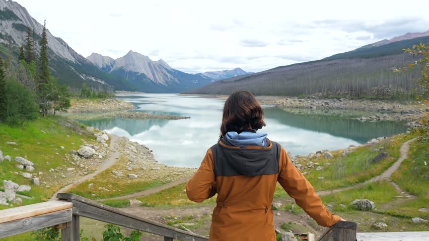 Majestic mountains encircling medicine lake while woman descending wooden stairs, savoring serene wilderness view in jasper national park