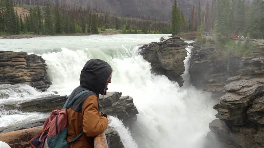 Backpacker enjoys the breathtaking view of athabasca falls, a powerful waterfall located on the athabasca river in jasper national park, a renowned unesco world heritage site