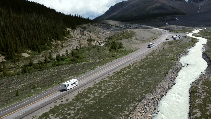 Driving along scenic icefields parkway near athabasca glacier, camper van and cars traverse glacial river with rocky mountain landscape in jasper national park, alberta, canada
