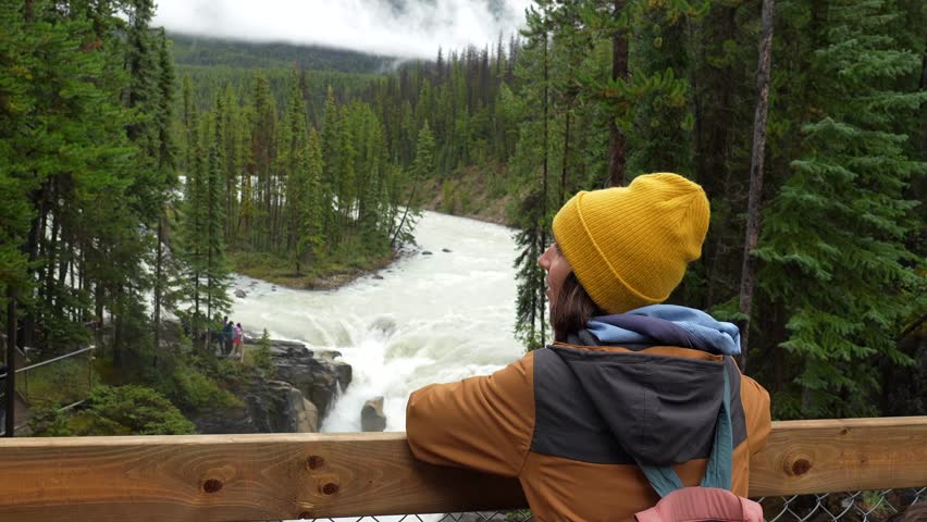 Sunwapta falls, located on the icefields parkway in jasper national park, captivates a tourist who is gazing at its powerful cascade amidst the lush evergreen forest