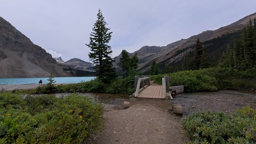 Picturesque views of bow lake in banff national park showcase a wooden bridge and a hiking trail amidst lush greenery, offering a serene escape in the canadian rockies