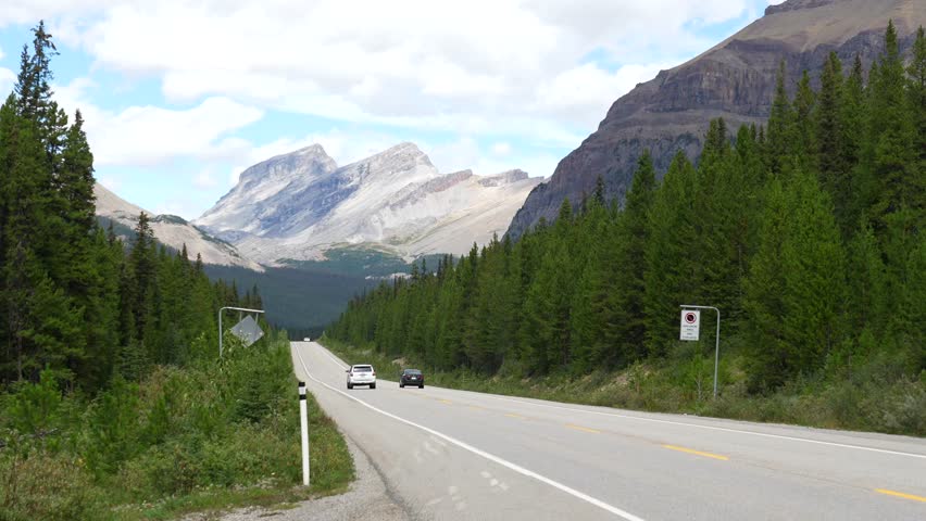 Majestic mountains and lush forests frame highway 93 as cars traverse the scenic route in banff national park, offering a captivating view of the canadian rockies