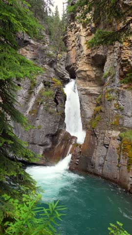 Majestic waterfall cascading into a vibrant turquoise pool, surrounded by lush greenery and rocky cliffs in johnston canyon, banff national park, canadian rockies, alberta, canada