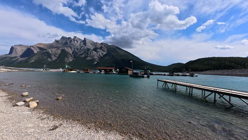Wooden pier stretching into turquoise waters of lake minnewanka with mount inglismaldie towering above in banff national park