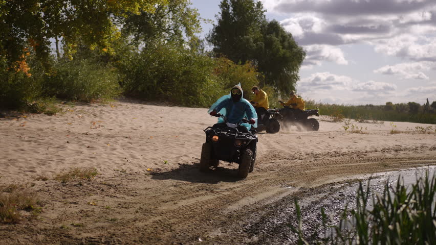 Riders on AVTs race shoreline, kicking dust across sandy riverbank with bluejacket leader carving tight turns while yellowjacket follower pushes
