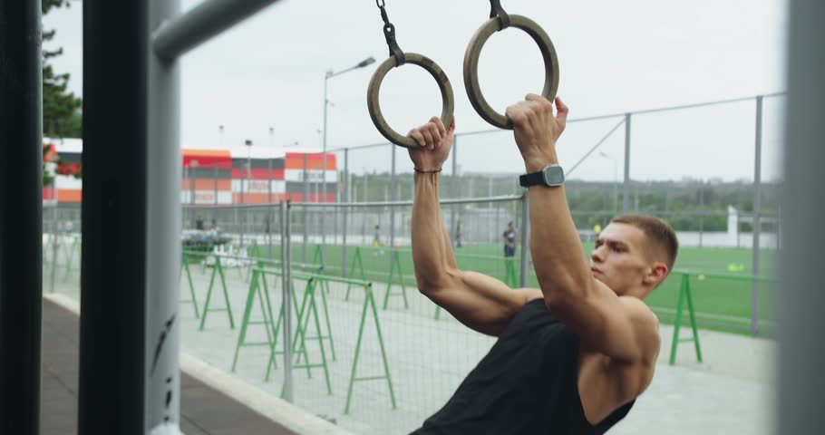 Man building arm muscles with exercise. Fitness Sport Street Workout. Muscle Up In Public Gym. Outdoors gym. Sportive fit man doing fitness exercises on sports rings. gymnastic rings.