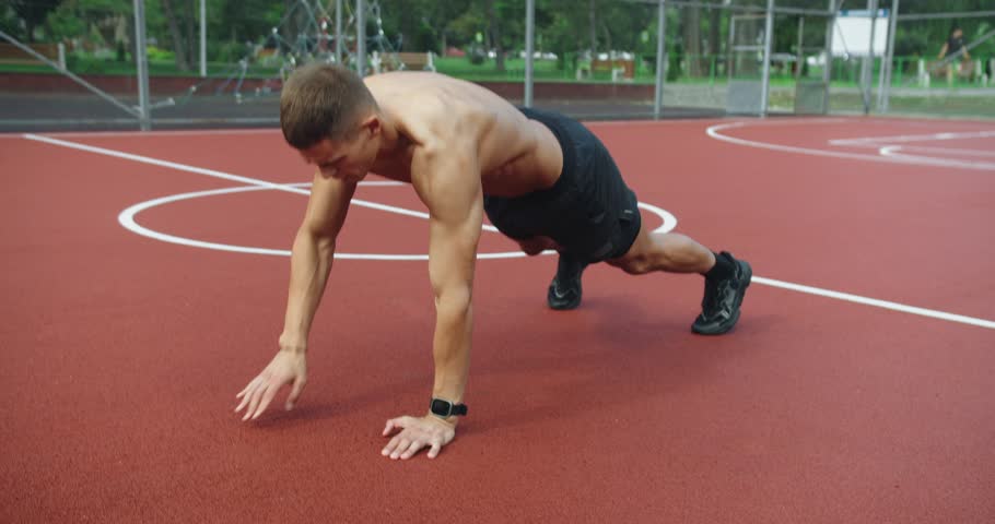 Athletic man has intense workout outdoors and doing cross fit training. Outdoor Fitness Park. Muscular man has cross fit training and doing plank exercise with shoulder tap outdoors at sports ground.