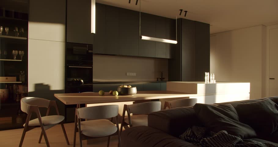Modern kitchen interior with dark green cabinets, white countertop, and wooden dining table. Sunlight streams through the window, illuminating the room.