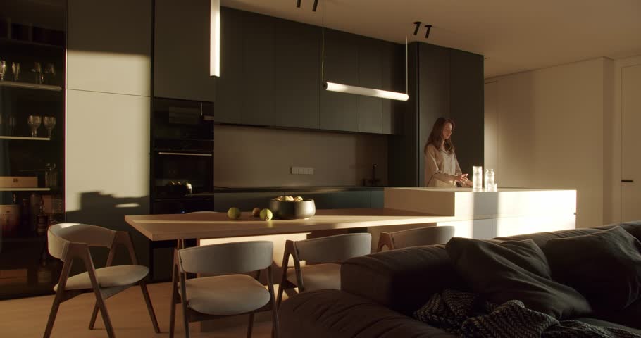 Modern kitchen interior with dark green cabinets, white countertop, and wooden dining table. Sunlight streams through the window, illuminating the room.