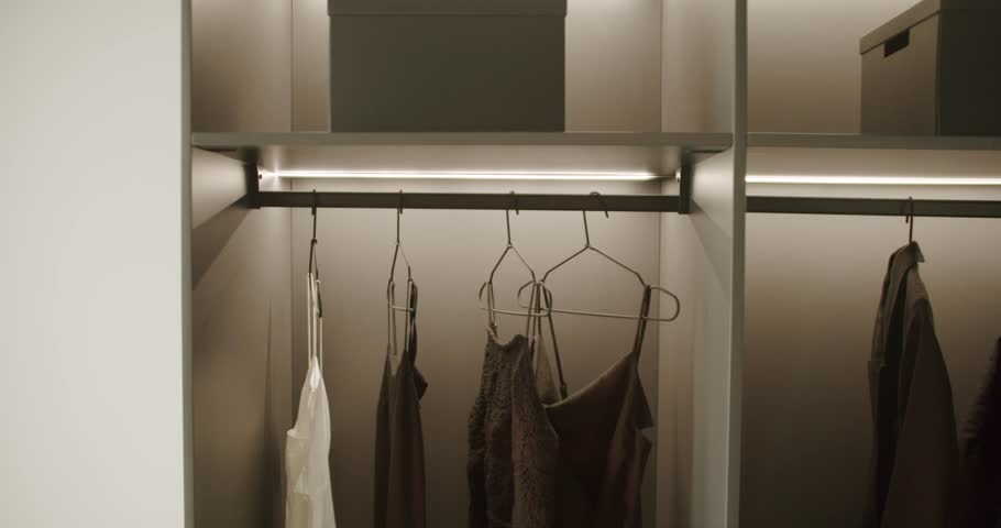Clothes hanging in a modern and minimalist walk-in closet or wardrobe. Neutral tones and soft lighting create a cozy and organized atmosphere. Perfect for fashion, lifestyle, interior design