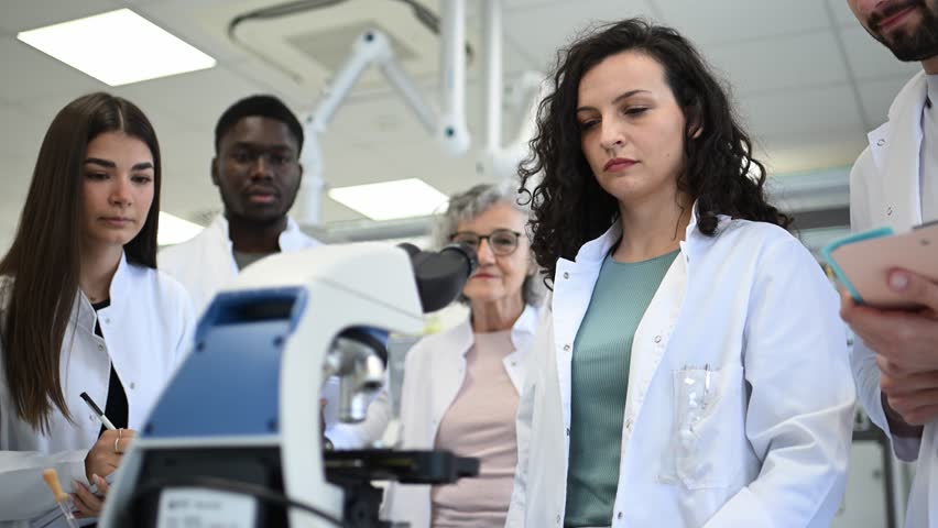 Young multiracial group of university students practicing with a microscope in a laboratory, guided by their female professor