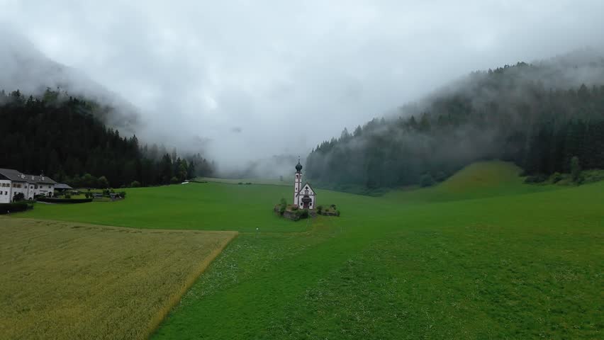 secluded mountain chapel, mist rolls over hillside shrine, quiet rural sanctuary nestled among lush green hills, serene mountain pasture with misty surroundings and aged wooden cross